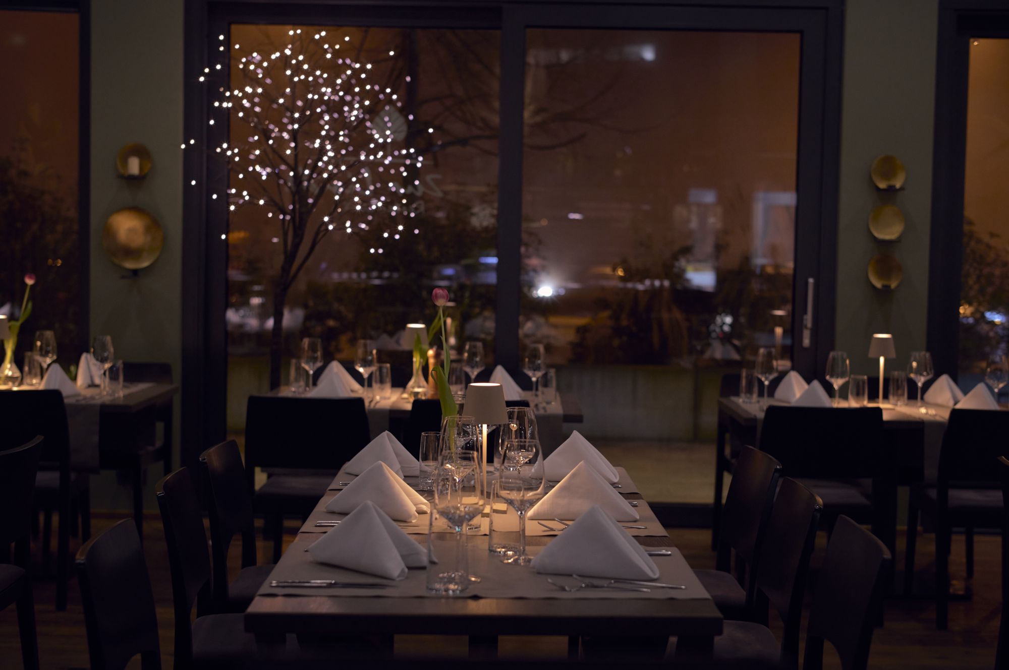 Warm evening light over set tables in the Zur Linde dining room, candles and glassware catching the glow.