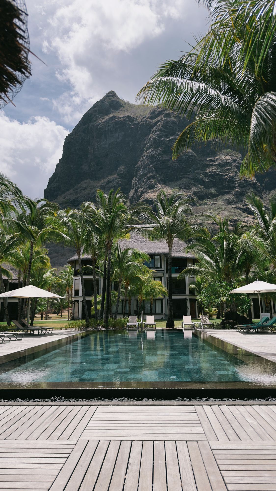 Infinity pool meeting the sea at dawn with the green peak of Le Morne rising beyond, Mauritius.