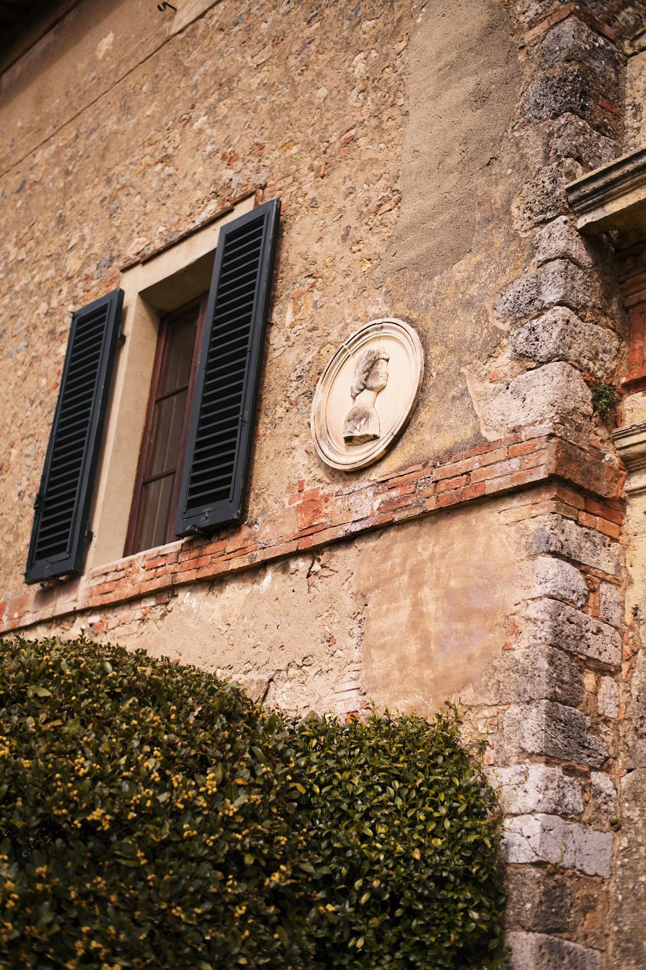 Weathered stone wall framed by ivy and a carved emblem at a Tuscan villa.