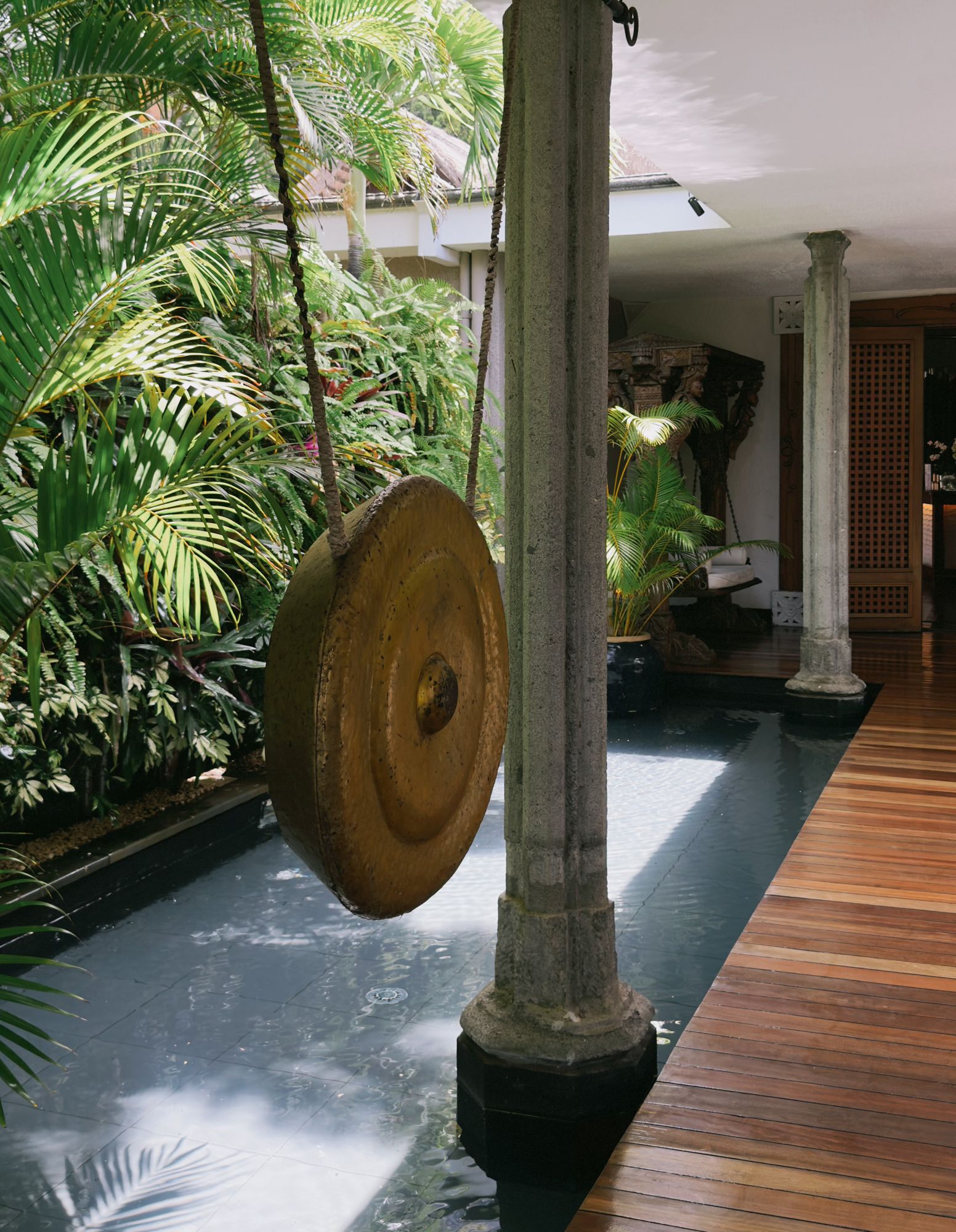 A bronze gong hanging in a tropical walkway, morning light on stone and timber, Mauritius.