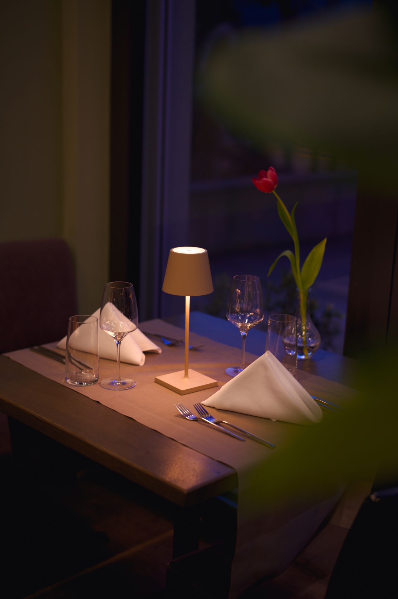 An intimate table for two at dusk, a table lamp and a single tulip against the window at Zur Linde.