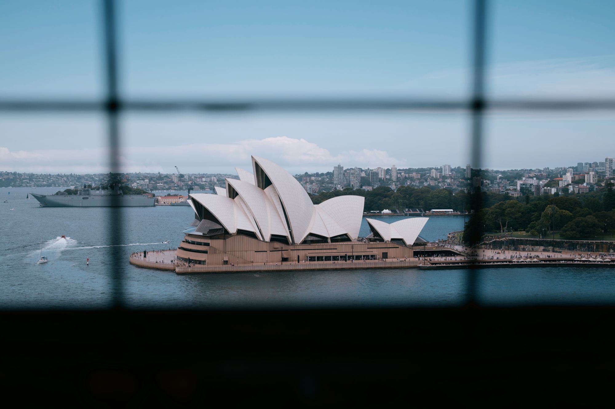The Sydney Opera House framed through the horizontal louvres of a window, harbour beyond.