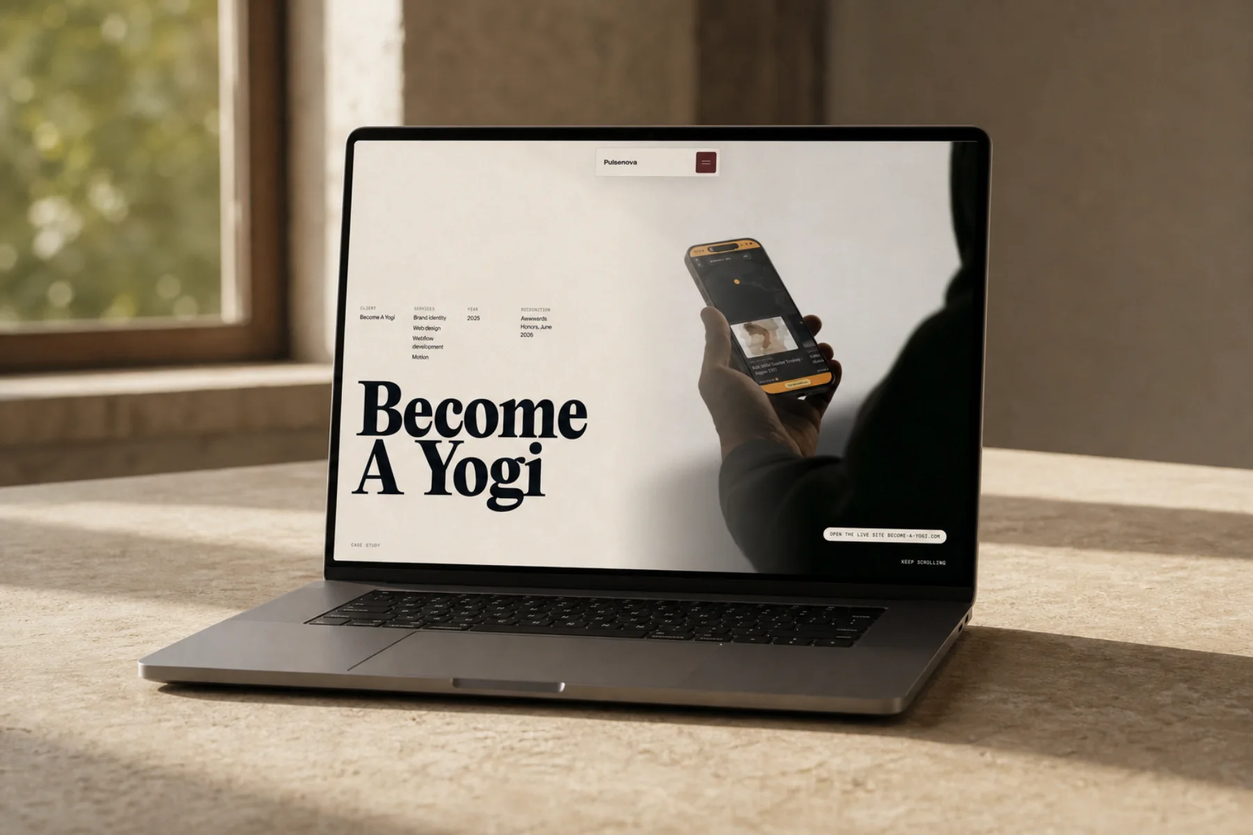 A laptop on a table by a window showing the Become A Yogi homepage